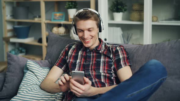 Cheerful Student Is Using Smartphone Looking at Screen and Laughing Having Fun and Listening