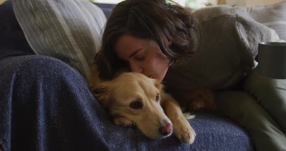 Smiling caucasian woman kissing her pet dog sitting on sofa at home