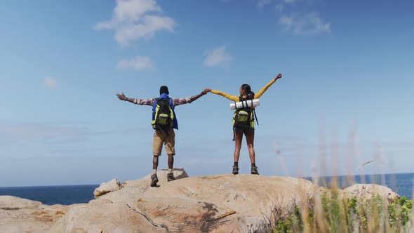 Rear view of african american couple standing on the rocks with arms wide open while trekking