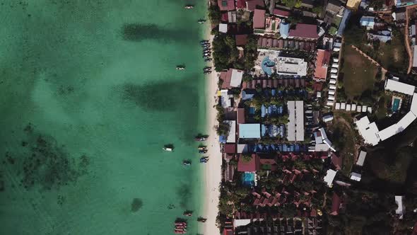 Aerial: Long tail boats on a beautiful beach with a village view.