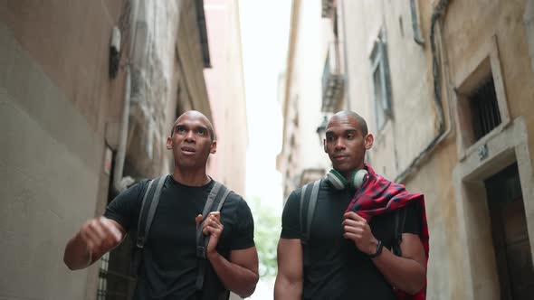 Two serious bald African brothers walking and pointing to the side on the street