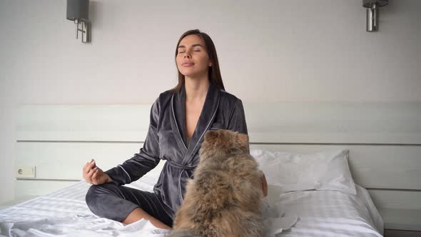 Young Beautiful Caucasian Woman Sits in the Morning on the Bed in Pajamas in the Lotus Position and