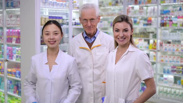 Positive Smart Senior Pharmacist Crossing Hands Looking at Camera Smiling Standing Indoors with