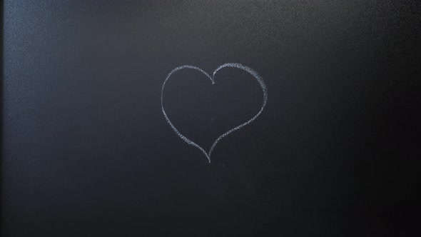 Hand draws heart icon on chalkboard