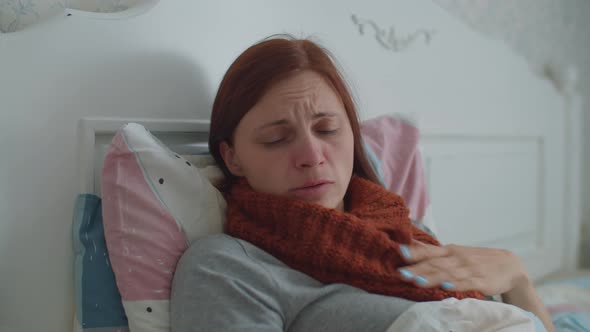 Sick Young Woman Laying in Bed Holding Cup of Hot Tea with Lemon in Hands. Woman with Warm Scarf on