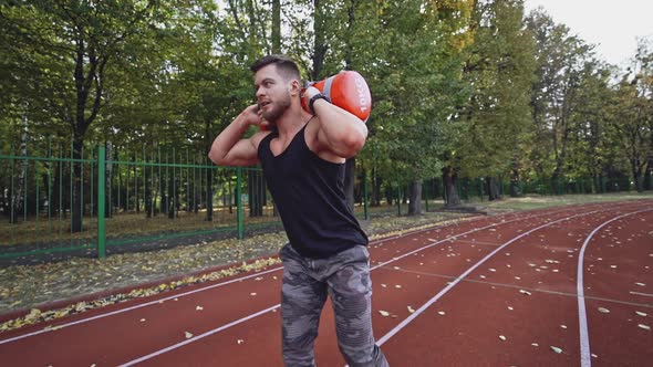 Male bodybuilder having his workout outdoors. Handsome athlete lifting 10 kg weights 