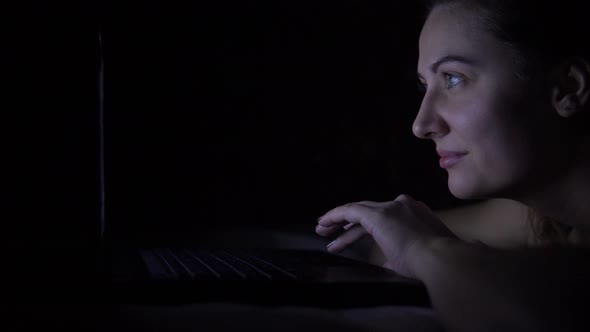 Attractive Girl Lying on Bed Using Laptop in Dark Room. 