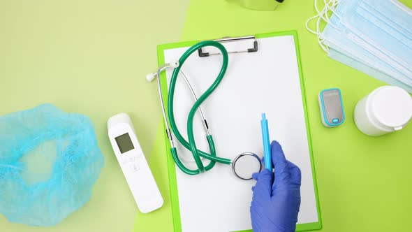 Hand in a blue latex glove puts medical supplies on a green table