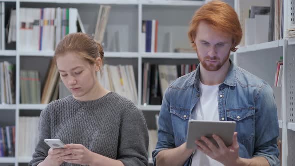 Redhead Man Using Tablet and Woman Using Smartphone in Office