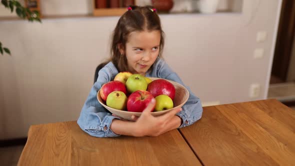 greed Little happy girl hold bowl with fruits in the kitchen at home