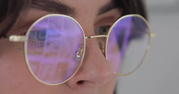 Woman working at laptop at night. The monitor screen is reflected in the glasses