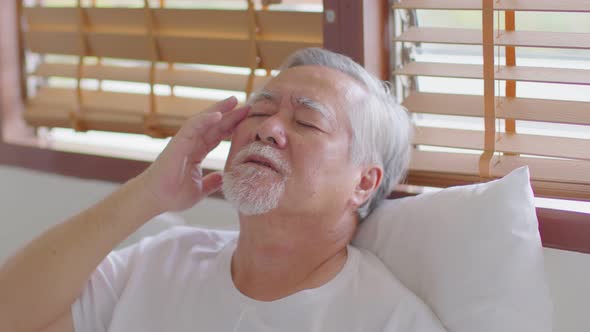 Asian Elderly senior man sudden headache and migraine so pain and illness on bed alone