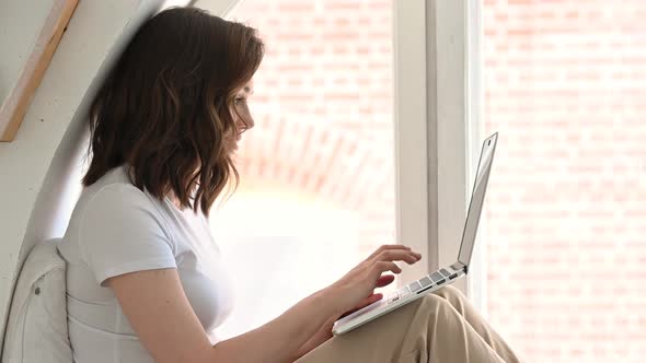 Young Attractive Girl with Her Bright Apartment Enjoying the Morning Using a Laptop