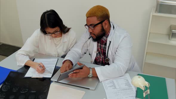 Male Doctor Showing His Female Trainee How To Fill in Forms Using Tablet