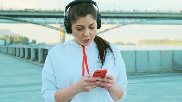 A Beautiful Girl in a White Sweater and Headphones Is Preparing for a Morning Run