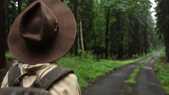 Blonde woman in hat with backpack in rainy forest