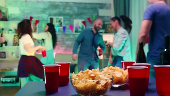 Young Woman at a Party with Neon Light Taking Chips From the Table and a Cup of Beer