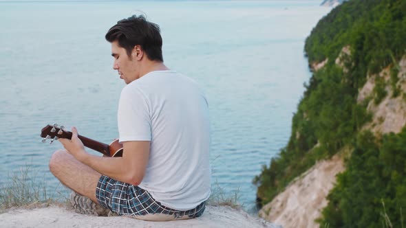 Young Man Playing Ukulele and Singing  Sitting on the Mountain