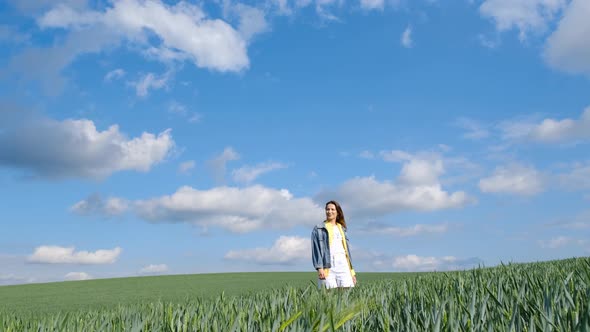 A Beautiful Lonely Girl Stands in the Middle of a Green Field with Her Arms Outstretched