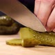 Hands is Cutting a Pickled Cucumber with a Knife on Wooden Board Closeup - VideoHive Item for Sale
