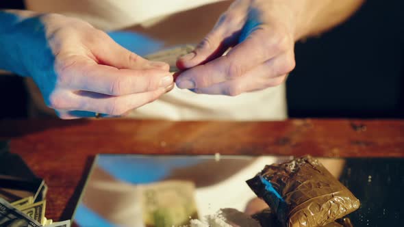 Abuse of drugs. Young addict's man sniffs and snorts a line of cocaine with a roll of banknote