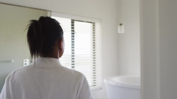 Rear view of mixed race woman in bathroom taking bathrobe off