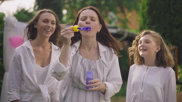 Positive Pregnant Woman Blowing Soap Bubbles Having Fun on Baby Shower Party with Daughters