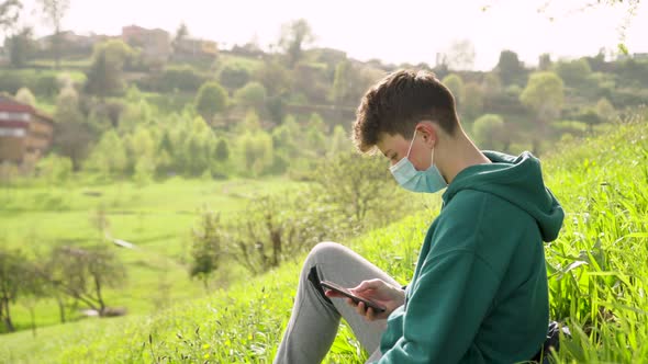 A teenager uses a smartphone while sitting on the grass in nature.