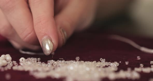 a seamstress with a golden manicure puts transparent round beads on a needle