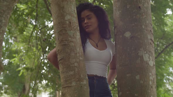 pan left of a curly hair latina girl in the middle of two tree trunk and smile