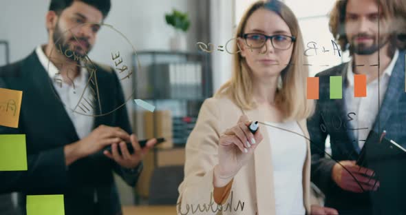 Woman Drawing Graphs on Glass Wall for Her Male Colleagues Work with them Over Start Up Project