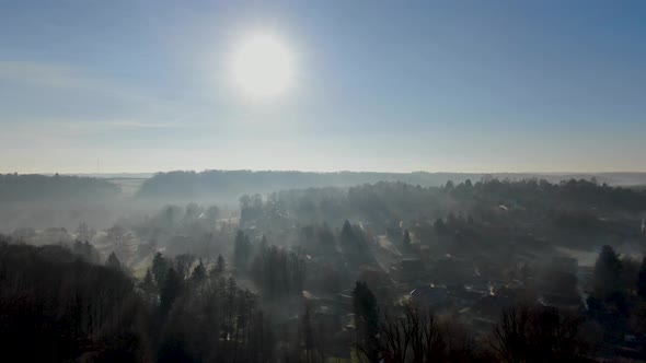 Aerial View of Forest and Farmland During Foggy and Cold Winter Morning with Blue Sky Facing the Sun