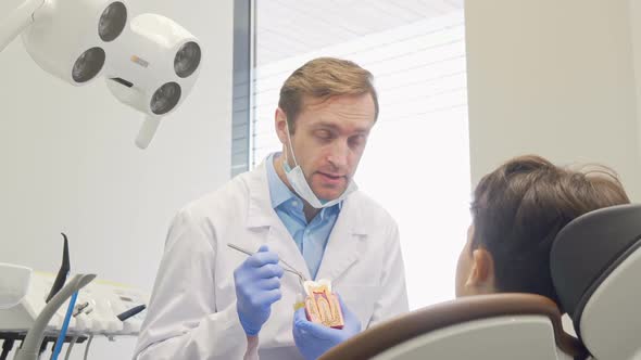 Cheerful Mature Male Dentist Smiling To the Camera While Educating Little Patient