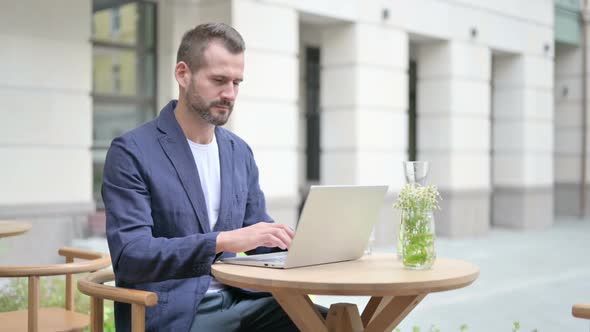 Man Showing No Sign While Using Laptop Sitting in Outdoor Cafe