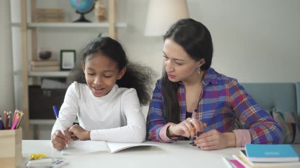 Medium Shot of Asian Happy Woman Tutor Teaching and Helping Her Black African American Girl Student