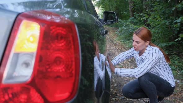 Young Woman Driver Looking at Scratch Damage of Her Car in the Forest. 