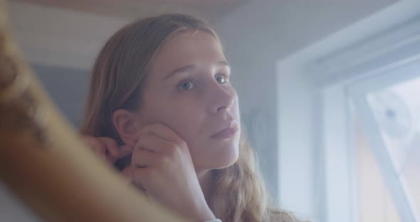 Reflection in the Mirror of a Beautiful Young Woman Putting On Her Earrings