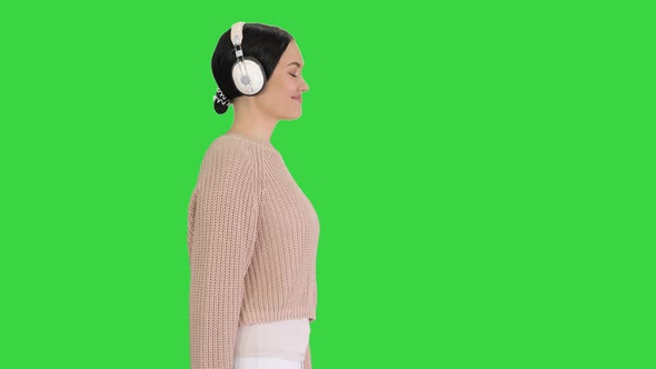 Young Woman with Headphones Walking Listening To the Music on a Green Screen, Chroma Key.