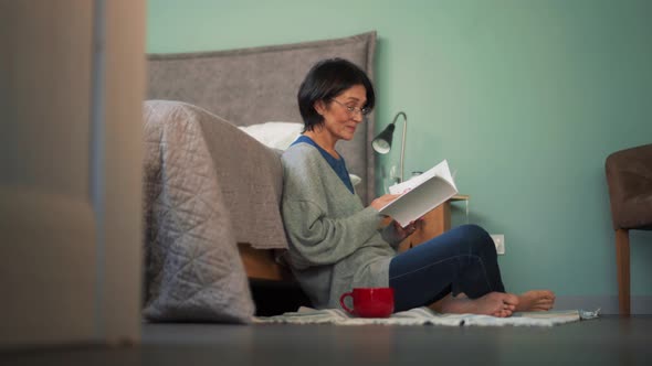 Positive mature woman reading book on floor