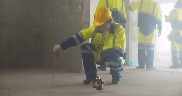 Manual Worker Using Laser Level Machine and Measuring Tape in Renovation Room