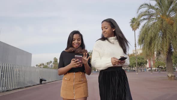 Girls walking in a city while using a mobile phone and laughing