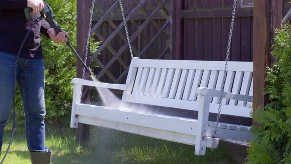 Male Gardener Removes White Paint From a Swing Bench with High Pressure Washer