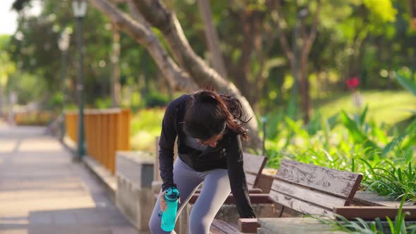 4K Asian woman drinking water from a bottle while jogging at public park in the morning.