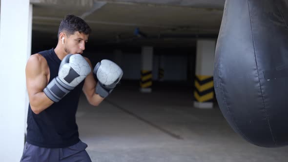 The Man Executes Strong Blows in the Boxing Bag at the Parking Zone Gym