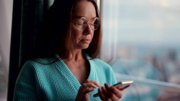 Pensive Nervous Woman is Typing Message in Mobile Phone Looking at Window and Sending Sms