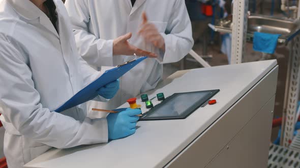 Workers in Protective Mask and Lab Coat with Clipboard Writing Down Data on Control Panel at Brewery