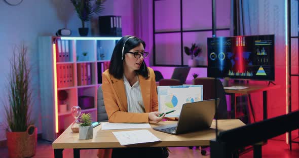 Female Office Manager in Headset Holding Video Chat on Computer and Explaining Report with Charts