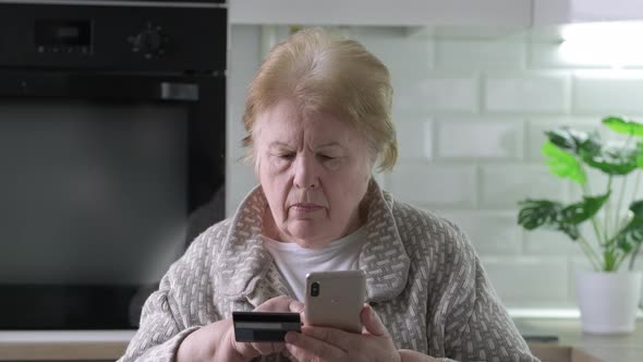 Serious Elderly Woman Shopping Online with Credit Card Using Mobile Cell Phone at Home