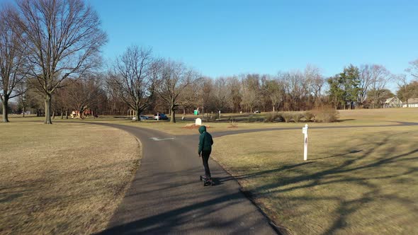 An aerial tracking of a man on an electric skateboard in an empty park on a sunny day. The drone fol