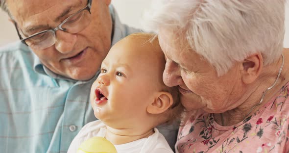 Elderly Couple Hold a Child on Their Lap Talk From Him Smile Raise His Hands